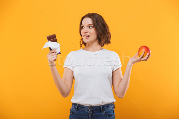 Emotional young woman holding apple and chocolate. Stock photo © deandrobot