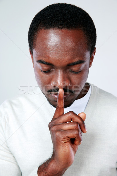 Portrait of african man with finger on lips over gray background Stock photo © deandrobot