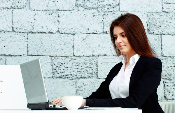 Young cheerful businesswoman sitting at the table in office near brick wall Stock photo © deandrobot