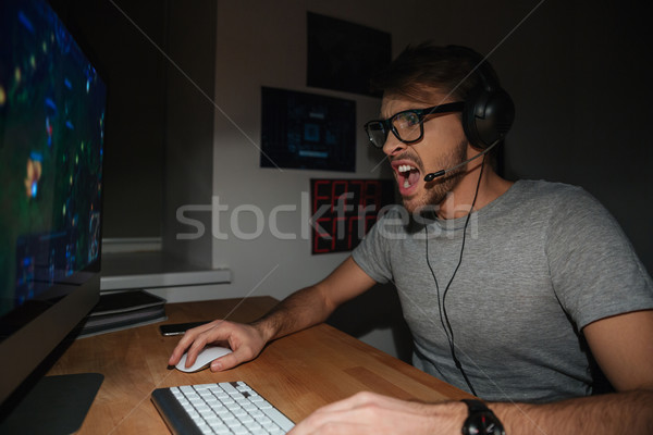 Excited gamer in glasses and earphones playing computer game  Stock photo © deandrobot
