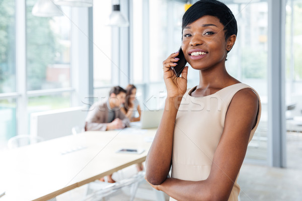 Happy businesswoman standing in office and talking on cell phone Stock photo © deandrobot