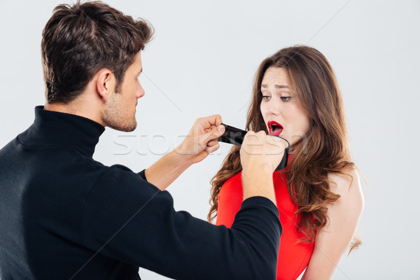 Criminal man covering mouth of scared woman with black tape Stock photo © deandrobot