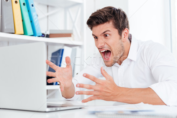 Furious angry young businessman working with computer and shouting Stock photo © deandrobot