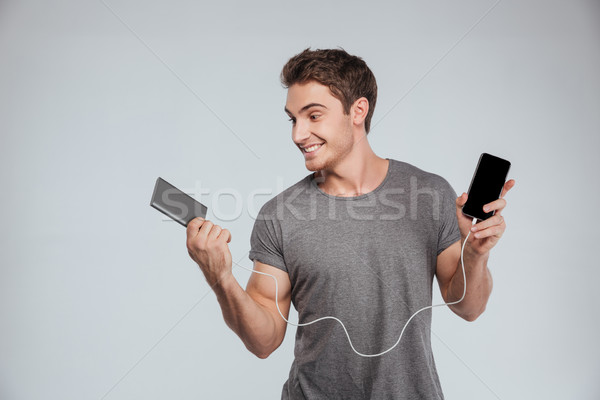 Stock photo: Portrait of a happy brunette man charging his mobile phone
