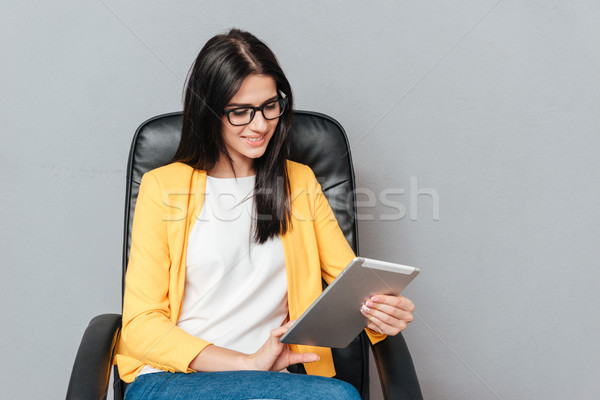 Stock photo: Cheerful woman sitting on office chair while using tablet computer