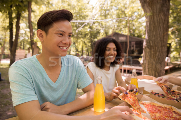 Smiling young multiethnic friends students outdoors drinking juice eating pizza. Stock photo © deandrobot