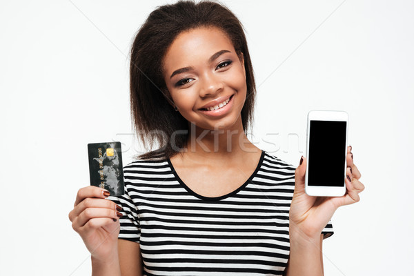 Stock photo: Happy young african lady using phone and holding debit card.
