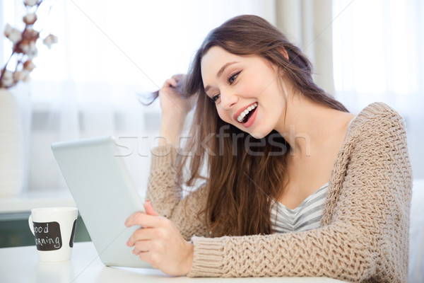 Attractive cheerful young woman using tablet  and laughing at home  Stock photo © deandrobot