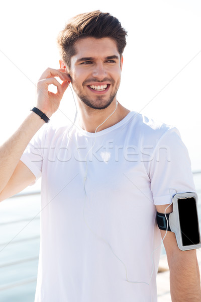 Handsome young sportsman listening music with earphones standing on pier Stock photo © deandrobot