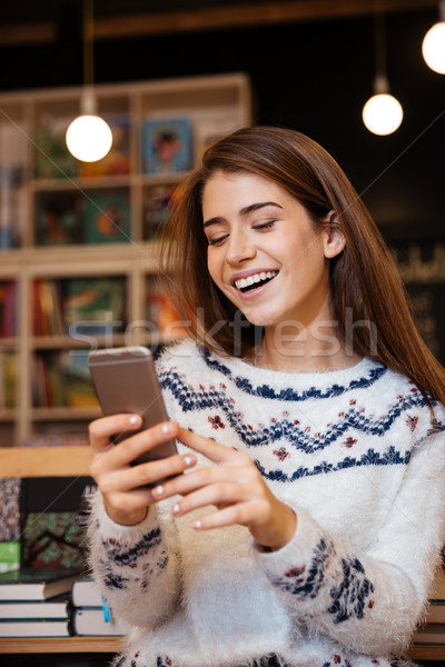 Pretty woman texting on mobile phone while sitting in library Stock photo © deandrobot
