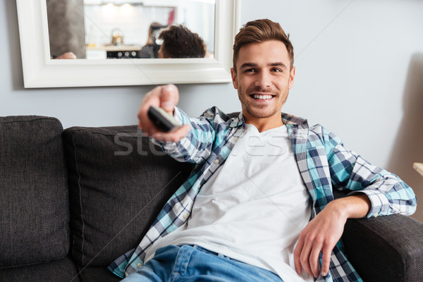 Smiling bristle man holding remote control while watching TV. Stock photo © deandrobot