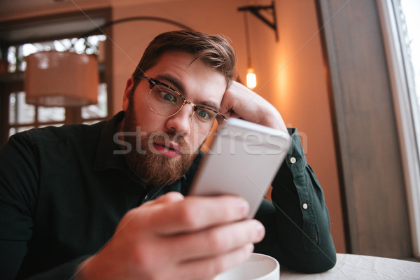 Shocked bearded young man using smartphone. Stock photo © deandrobot