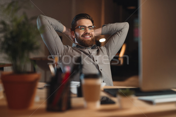 Happy bearded designer working at night and stretching. Stock photo © deandrobot