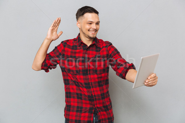 Smiling man using tablet computer and waving at camera Stock photo © deandrobot