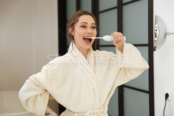 Happy young woman standing and brushing her teeth in bathroom Stock photo © deandrobot
