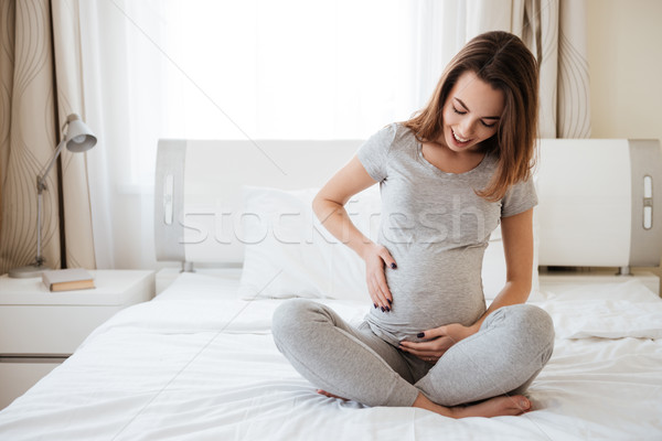 Wesoły kobieta w ciąży posiedzenia bed dotknąć żołądka Zdjęcia stock © deandrobot