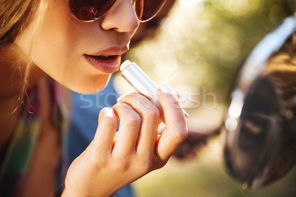 Woman sitting on scooter outdoors doing makeup of lips. Stock photo © deandrobot