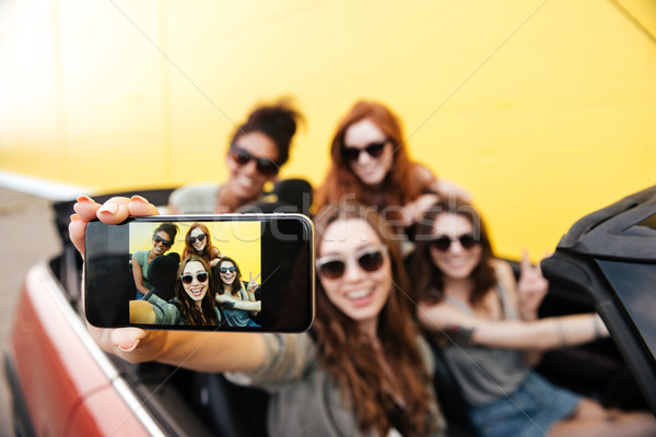 Smiling emotional four young women friends sitting in car Stock photo © deandrobot