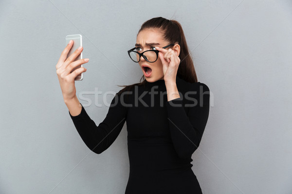 Retrato confuso mulher jovem óculos olhando telefone móvel Foto stock © deandrobot