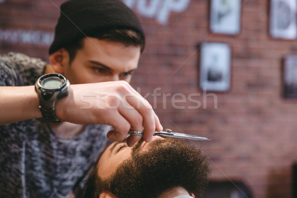 Young consentrated barber grooming beard of  man with scissors   Stock photo © deandrobot