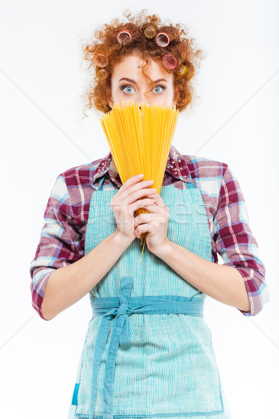 Amazed pretty housewife covered face with uncooked spagetti  Stock photo © deandrobot