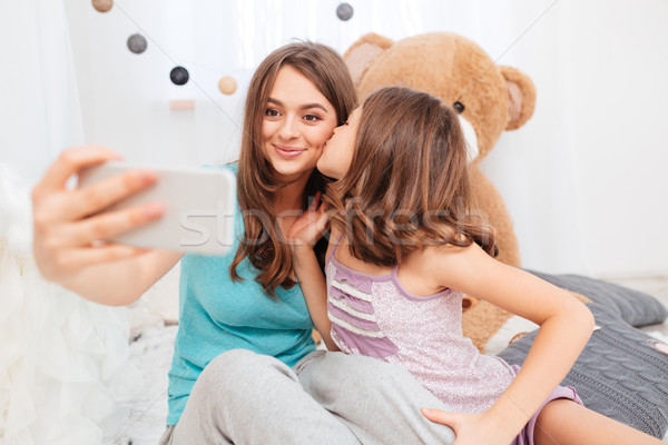 Two pretty smiling sisters kissing and making selfie  Stock photo © deandrobot