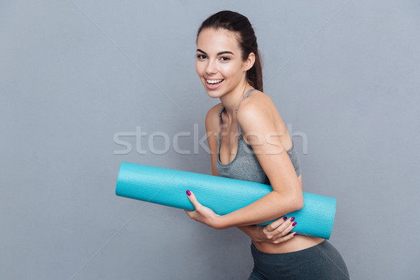 Attractive laughing sportswoman holding yoga mat isolated over grey background Stock photo © deandrobot