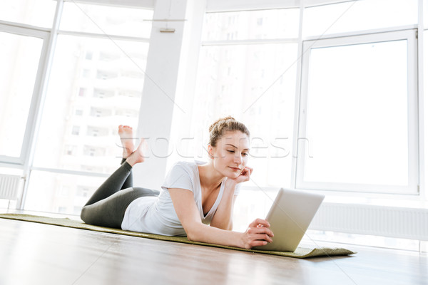 Beautiful young woman lying on yoga mat and using tablet Stock photo © deandrobot