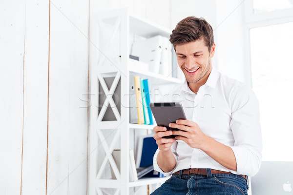Smiling young businessman sitting at the table and using tablet Stock photo © deandrobot