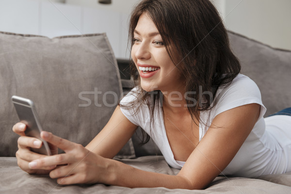 Woman lying on sofa and using cell phone at home Stock photo © deandrobot