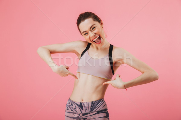 Joyful sportswoman pointing on her tummy and looking at camera Stock photo © deandrobot