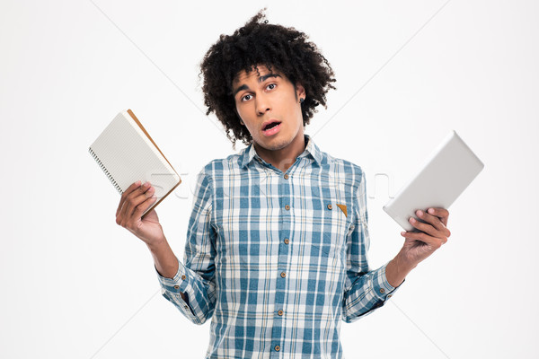 Afro american man choosing between paper book or tablet computer Stock photo © deandrobot