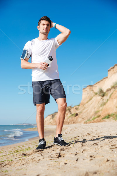 Attractive young sportsman with bottle of water on the beach Stock photo © deandrobot