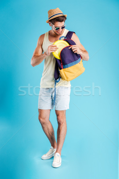 Happy young man standing and taking frisbee disk from backpack Stock photo © deandrobot