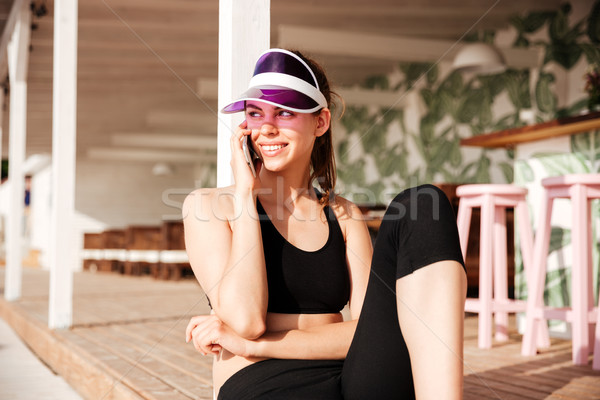 Young attractive sports woman talking on smartphone in cafe outdoors Stock photo © deandrobot