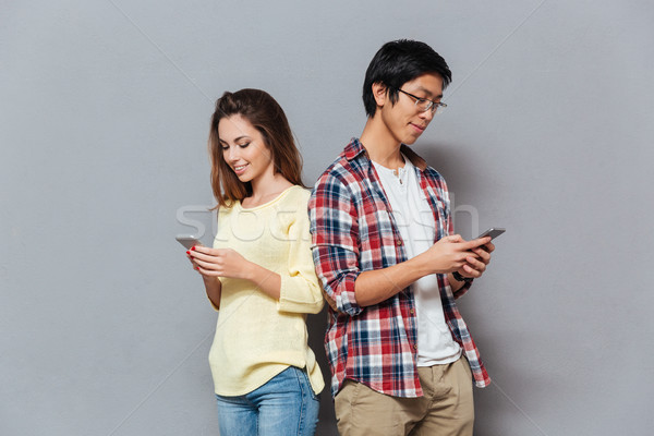 Portrait of an interracial couple standing and using mobile phones Stock photo © deandrobot