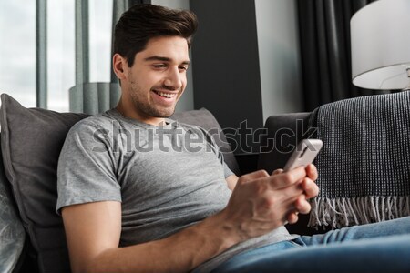 Young cheerful man looking at phone indoors Stock photo © deandrobot