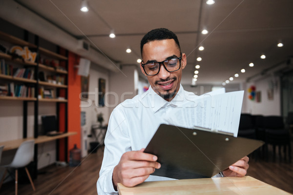 Happy african businessman looking at notepad. Coworking. Stock photo © deandrobot