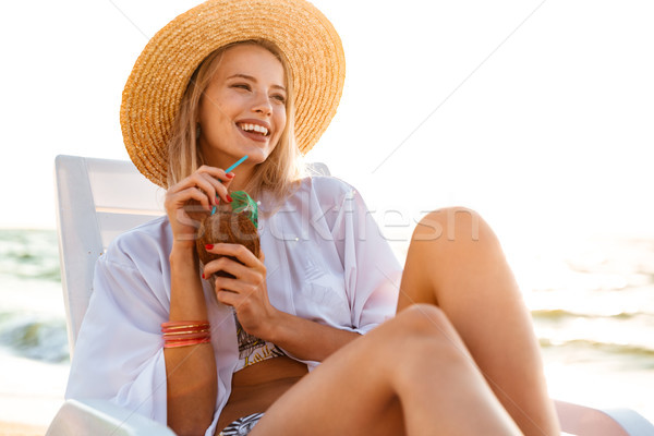 Photo of joyful blonde woman 20s in straw hat drinking exotic co Stock photo © deandrobot