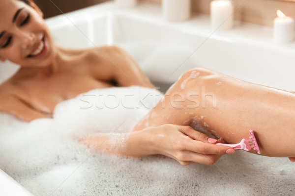 Beautiful woman in bathroom lies resting in bath shaving her legs. Stock photo © deandrobot