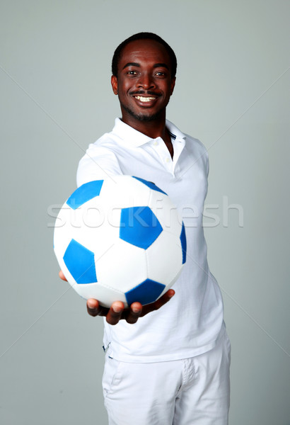 Happy african man giving a soccer ball at you on gray background Stock photo © deandrobot