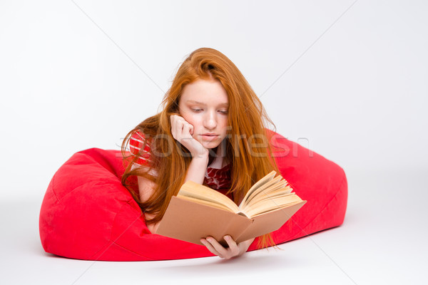 Concentrated girl relaxing in red bean bag and reading book Stock photo © deandrobot