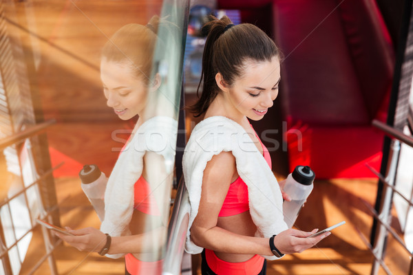 Smiling sportswoman drinking water and using smartphone in gym  Stock photo © deandrobot