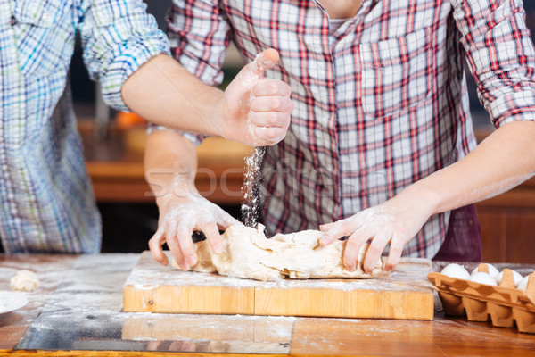Young couple adding flour and kneading dough on the kitchen Stock photo © deandrobot