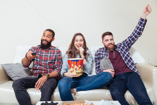 Friends eating popcorn and watching tv together Stock photo © deandrobot