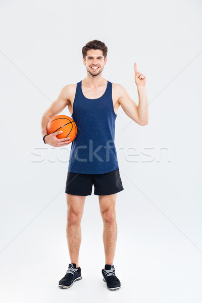 Smiling young sportsman holding basket ball and pointing finger up Stock photo © deandrobot