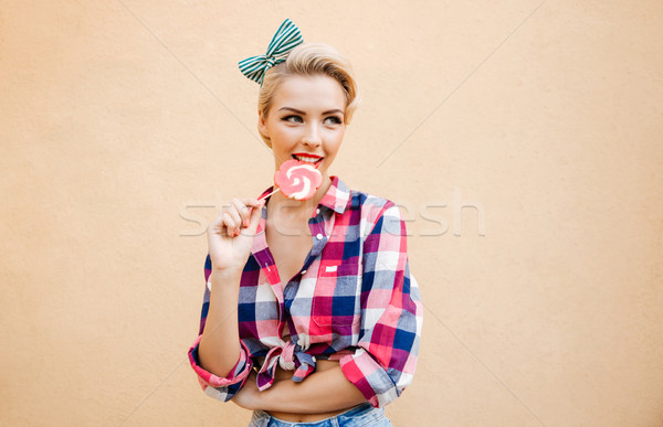 Happy cute pin up girl standing and eating colorful lollipop Stock photo © deandrobot