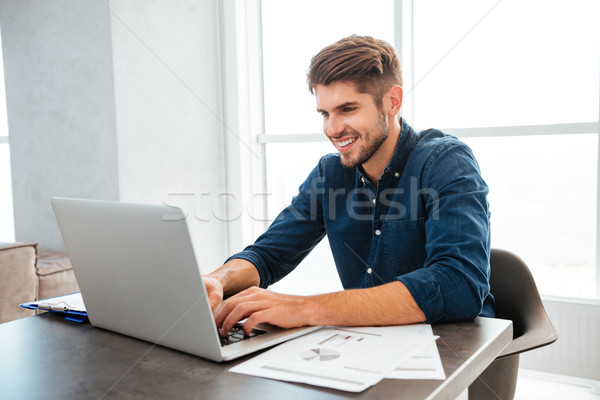 Giovani felice uomo utilizzando il computer portatile seduta tavola Foto d'archivio © deandrobot