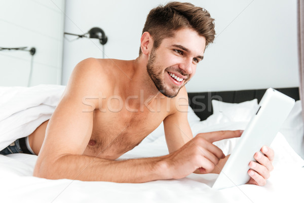 Happy handsome young man using tablet in bed Stock photo © deandrobot
