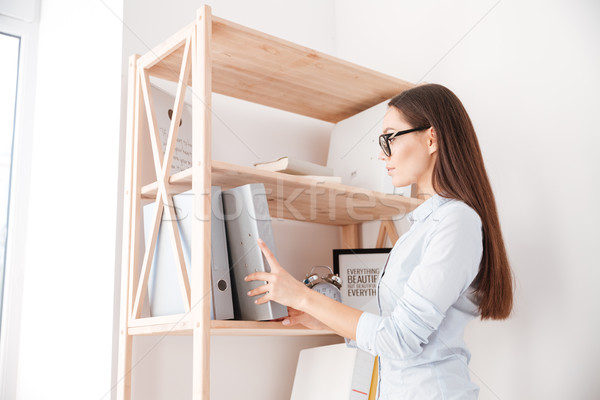 Businesswoman taking folder from book shelf Stock photo © deandrobot
